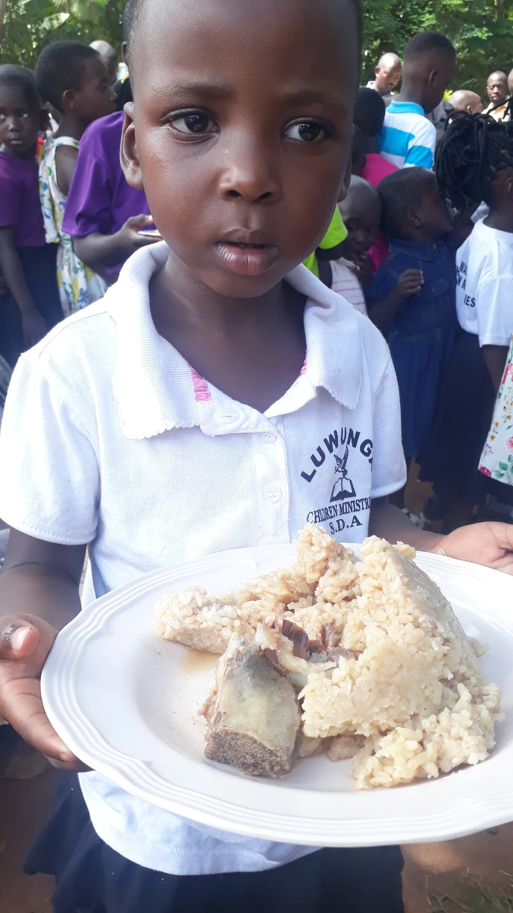 A child outdoors holding a plate of food.
