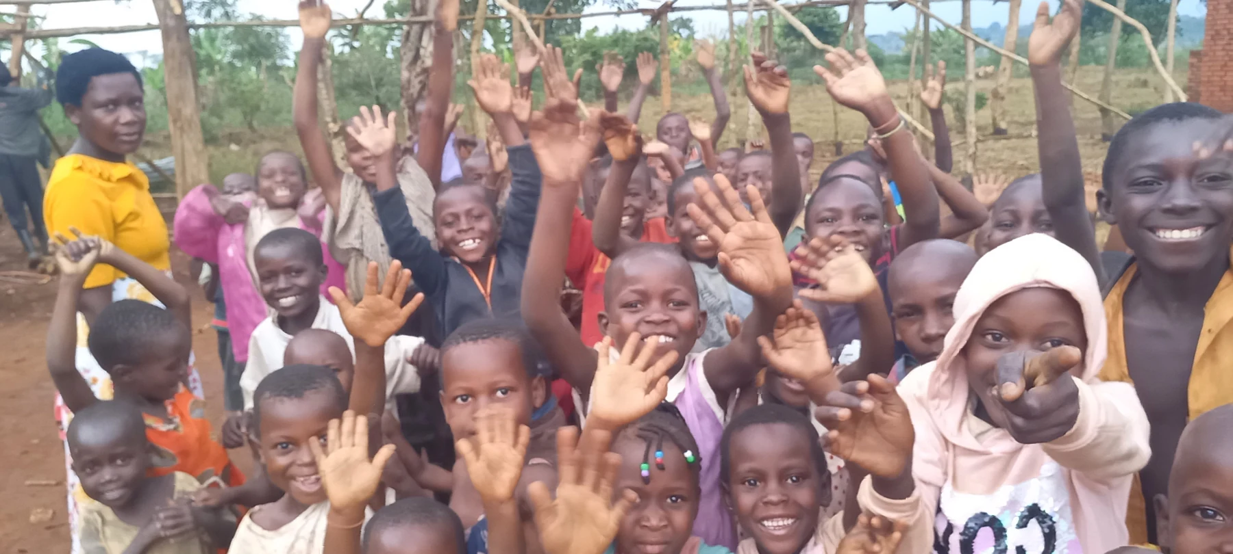 Children smile and raise their hands outdoors.